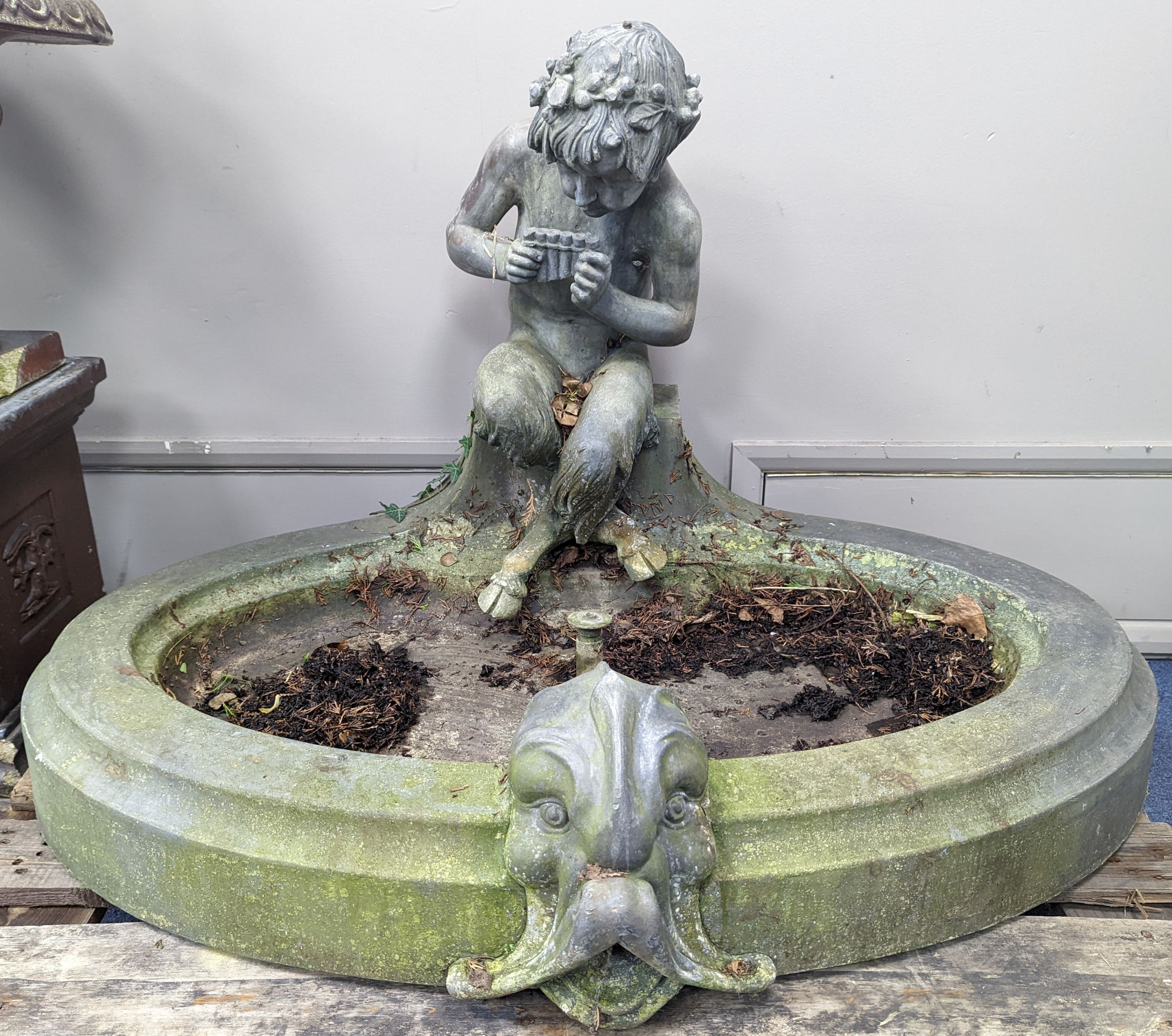An early 20th century oval lead garden fountain formed as a seated satyr playing pan pipes with stylised dolphin spout, width 120cm, depth 84cm, height 74cm